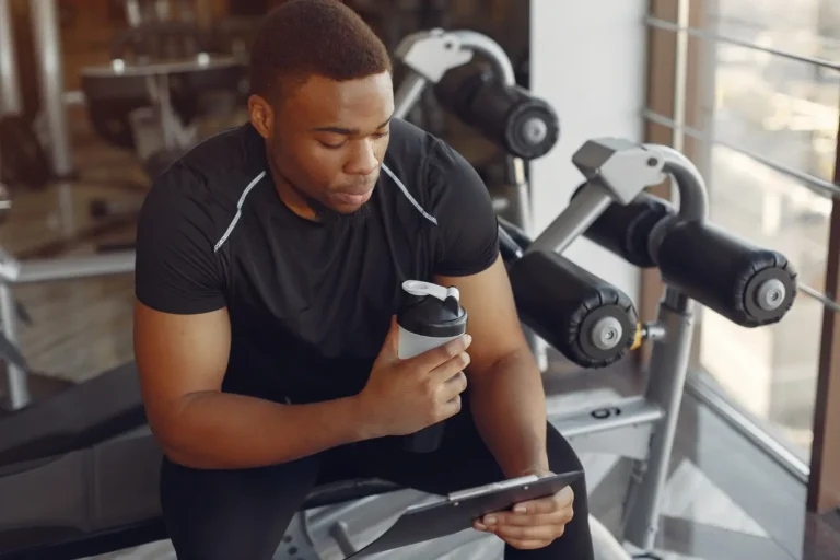 a man sitting on a bench holding a tablet and a bottle-Men's Health Coaching & Fitness Training